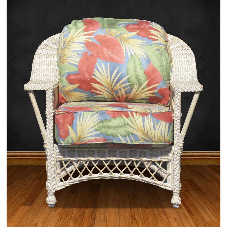 Front view of the Bar Harbor arm chair in whitewash with red, green and blue tropical leaf cushions on a wood floor