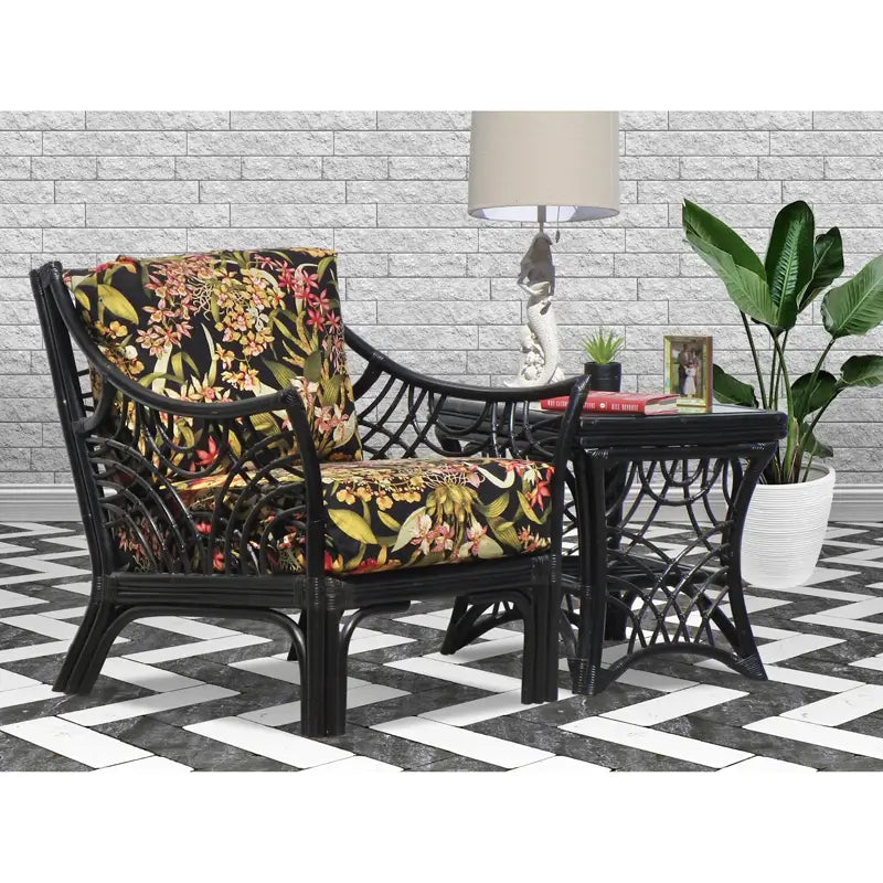 Black rattan lounge chair with black tropical orchid cushions beside a matching glass-top end table