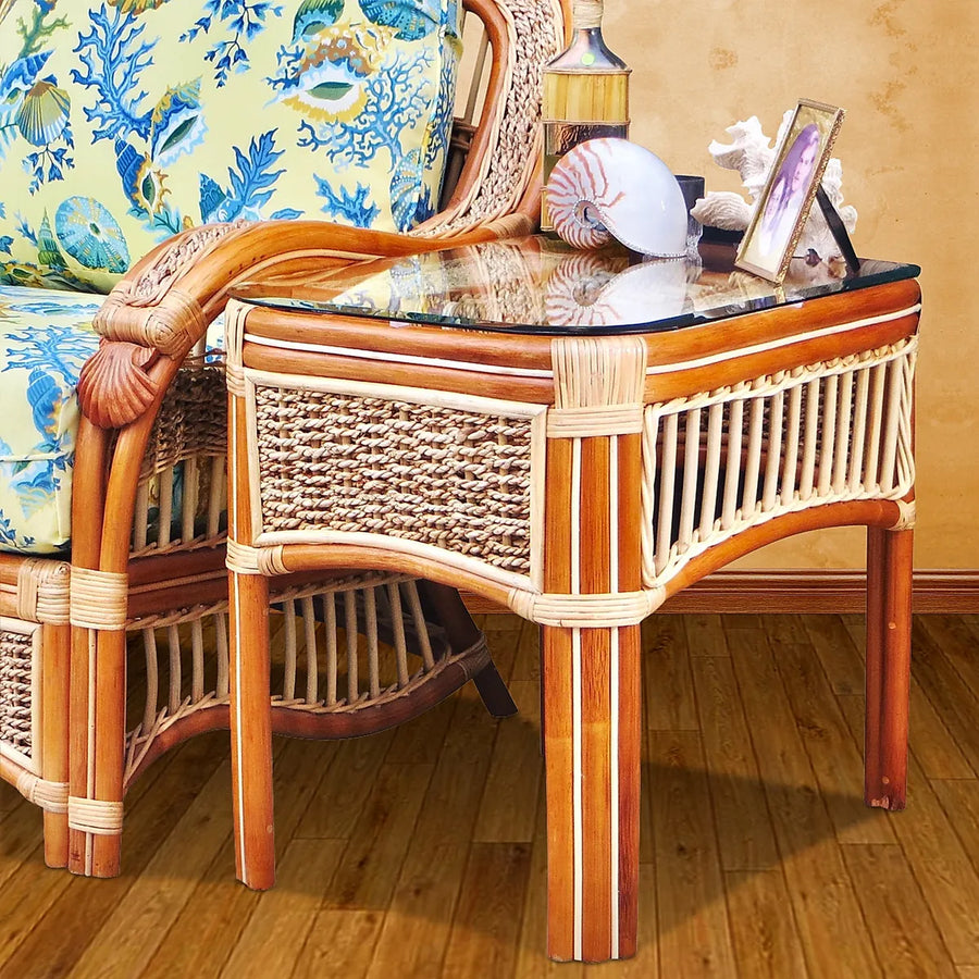 Seascape end table in natural with a glass top, shells and a framed photo, beside the arm chair's carved shell arm and sea print cushions