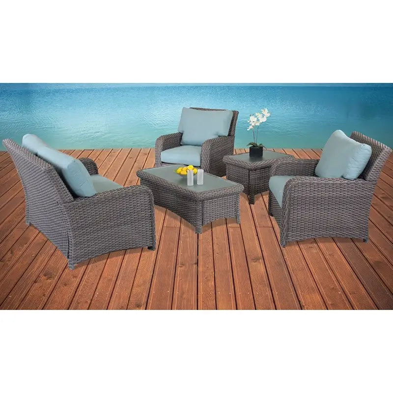 South Sea Rattan St. Tropez armchairs in Stone Gray finish with blue cushions and matching tables on a waterfront deck