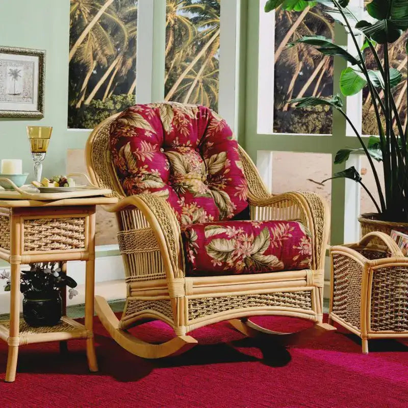 Indoor wicker rocking chair with red floral cushions in a sunroom, beside a matching end table and magazine basket
