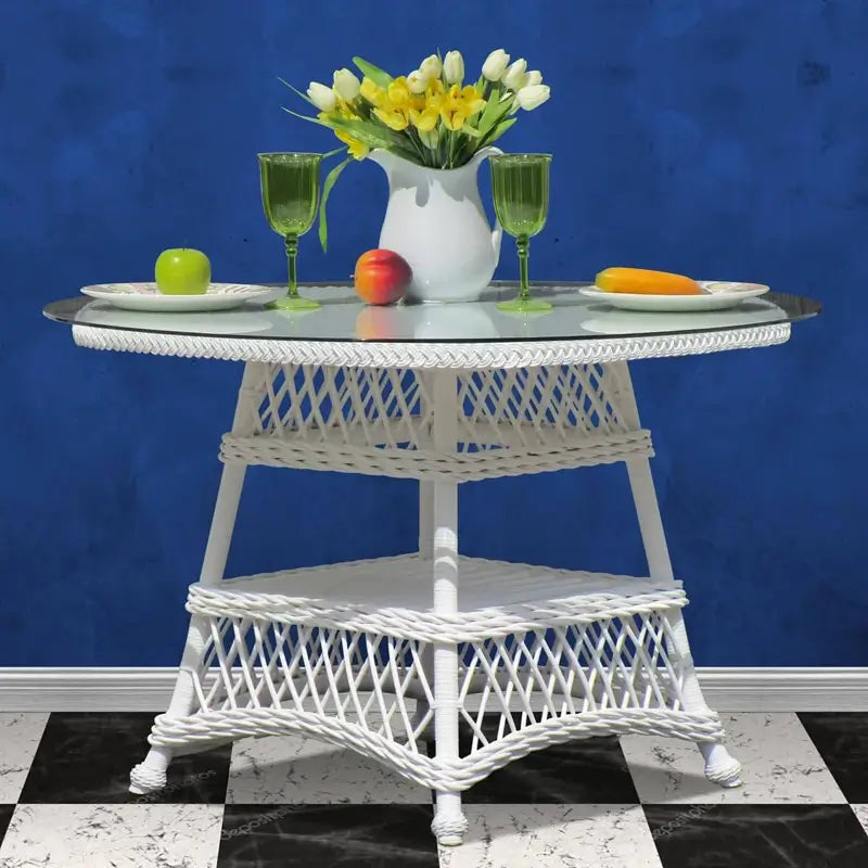 Bar Harbor round table in white wicker with a glass top, lattice base and woven lower shelf, set with plates and flowers
