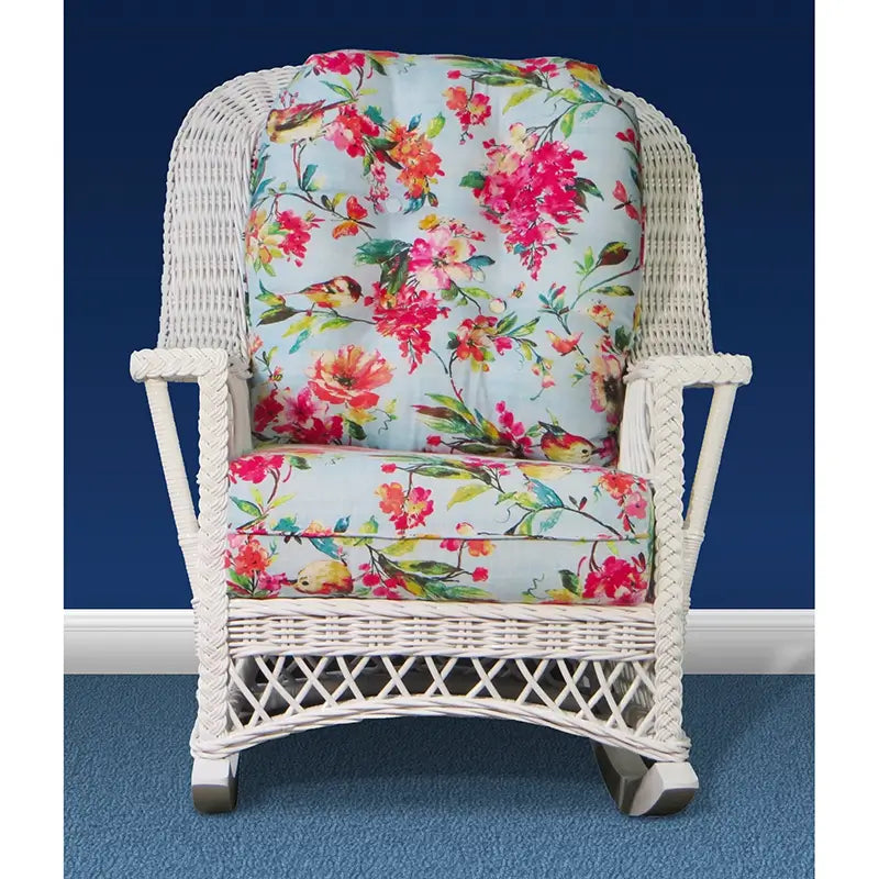 Front view of a white wicker rocker with braided arms, a lattice apron and floral cushions printed with birds and blossoms