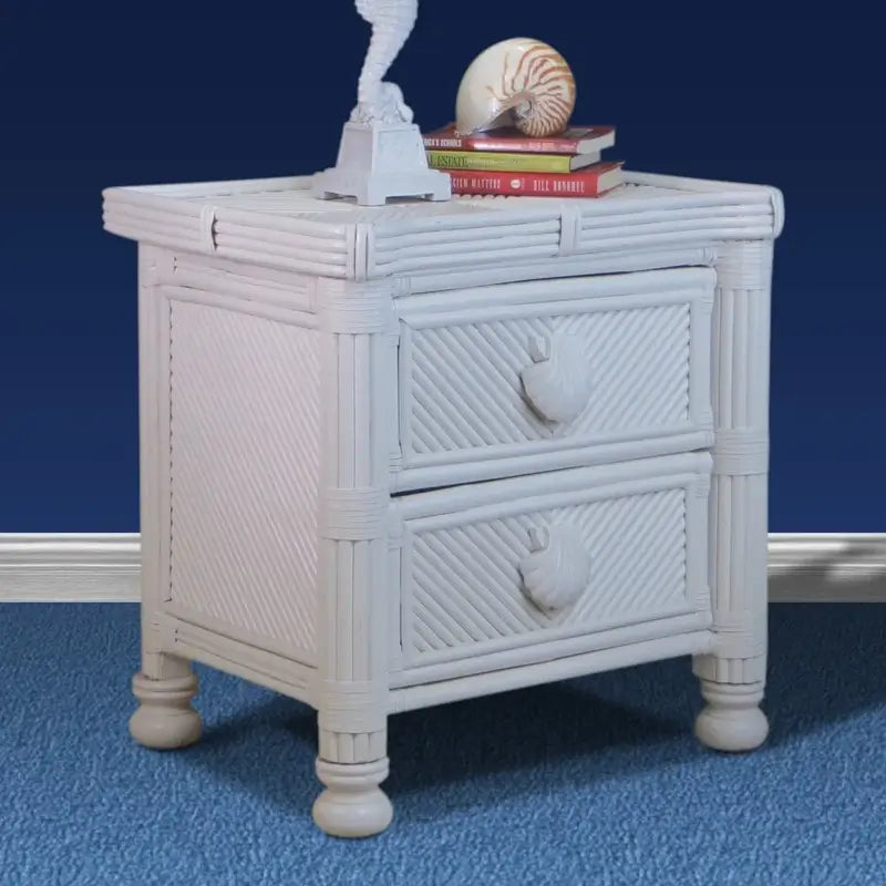 White wicker nightstand at an angle against a navy wall, showing the woven side panel and seashell drawer pulls
