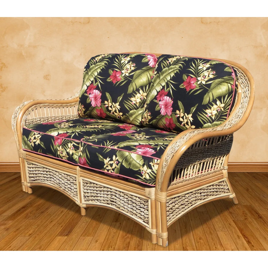 Islander natural wicker loveseat with black hibiscus print cushions, angled to show the curved arm and woven side