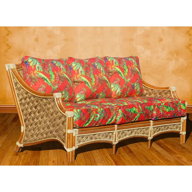 Natural wicker sofa seen from the front with three seat and three back cushions in a red leaf print, on a wood floor