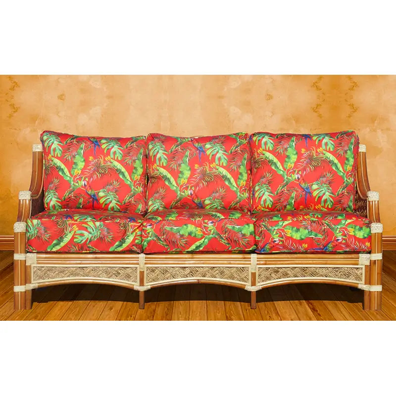 Natural wicker sofa seen from the front with three seat and three back cushions in a red leaf print, on a wood floor