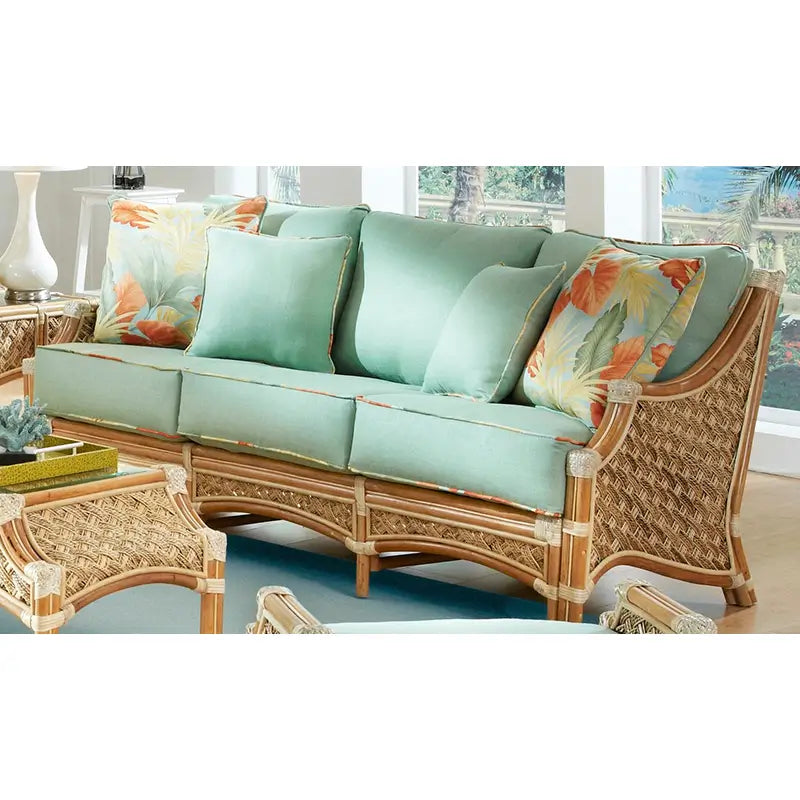 Wicker sofa with cushions in seafoam green and orange leaf-print toss pillows, set in front of a window