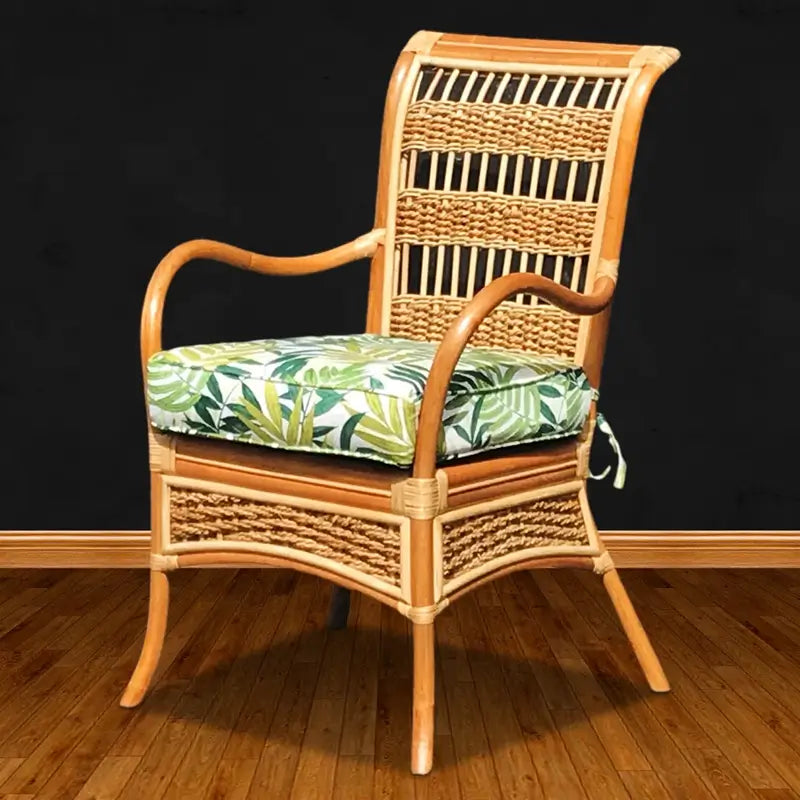Natural rattan dining chair with curved arms, a woven high back and a green palm leaf print seat cushion