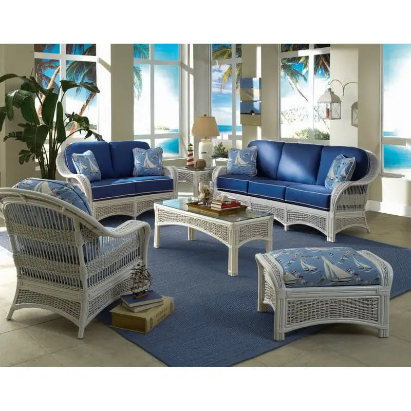 White wicker coffee table with a glass top and arched woven aprons in a sunroom, matching Regatta seating with blue cushions