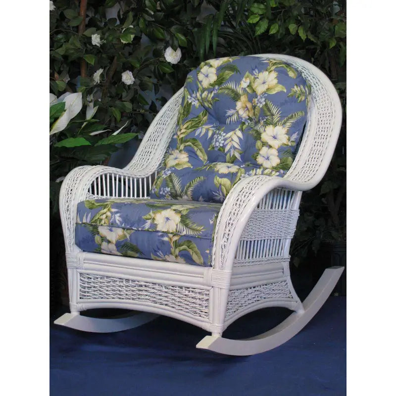Regatta white wicker rocking chair with blue and cream hibiscus cushions, set in front of leafy green plants