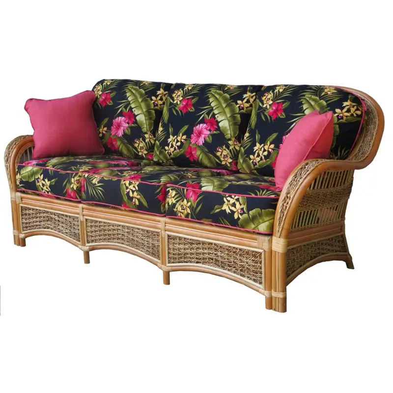 Spice Island wide arm sofa in natural rattan, three-quarter view, with black hibiscus print cushions and woven base panels