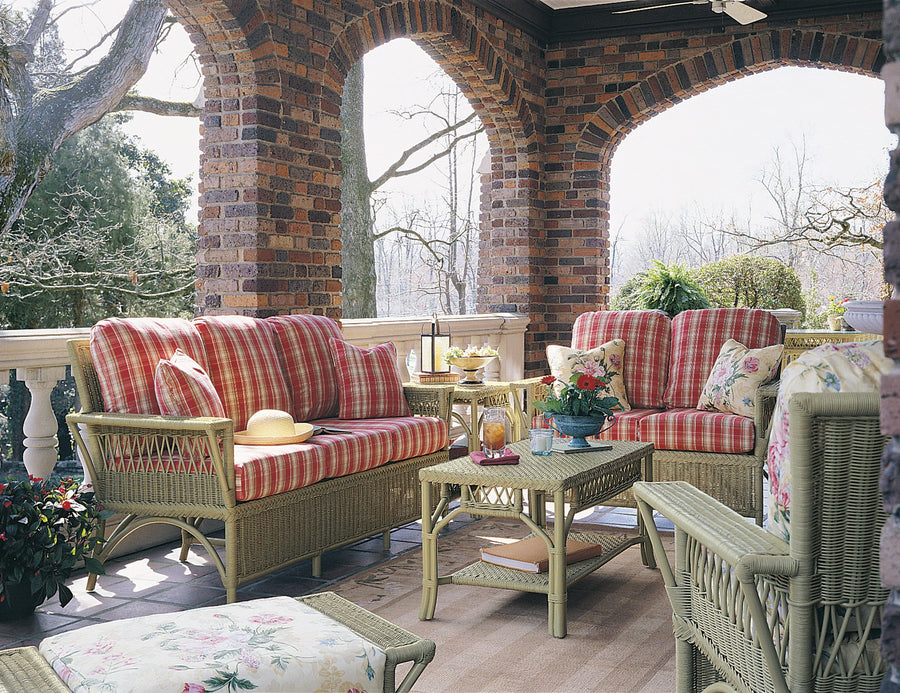 Windsor sofa, loveseat and coffee table in sage green with red plaid cushions on a brick-arched porch
